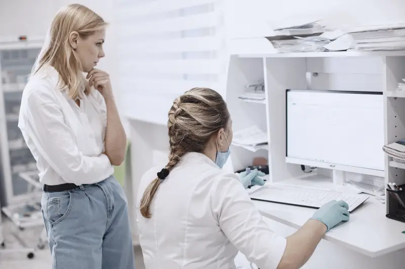 Twee zorgmedewerkers bekijken samen patiëntgegevens op een computer bij een kliniekbalie